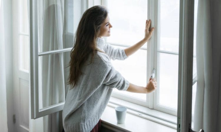 Woman is opening window to look at beautiful snowy landscape outside